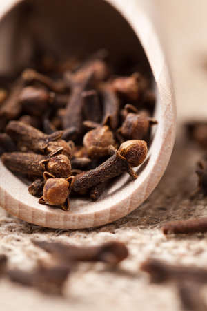 Brown dry clove aromatic spice scattered in wooden shovel on textile background close upの写真素材