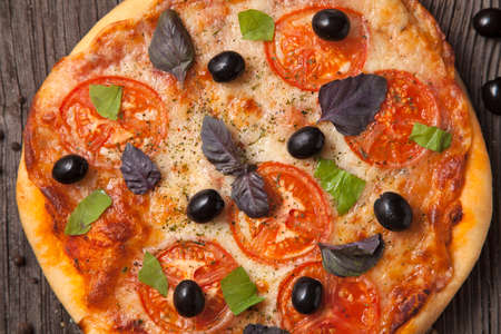 Italian pizza margherita with tomatoes, pepper, olives and basil on vintage rustic background close upの写真素材