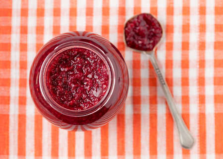 Jar of sweet berry jam with spoon on textile table background. Top view.