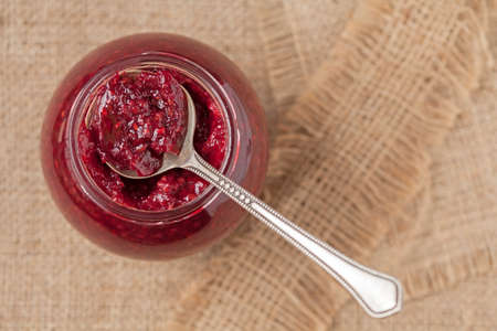 Jar of sweet berry jam with spoon on vintage textile background. Top view.
