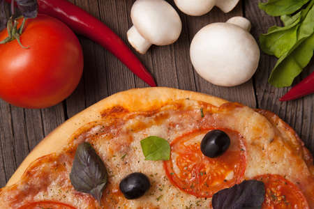 Pizza margherita with tomatoes, pepper, olives and basil on vintage rustic background close upの写真素材
