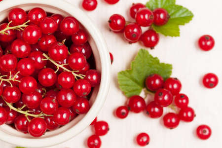 Red currant superfood in a bowl with green leaves on white background