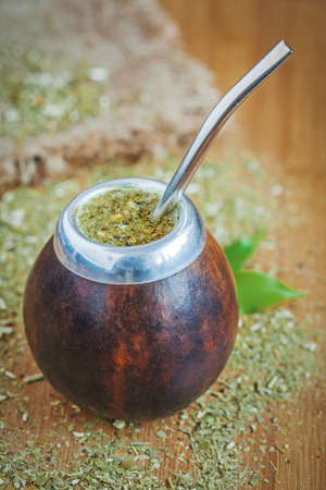 Latin traditional yerba mate tea in calabash with bombilla on wooden table background with green...