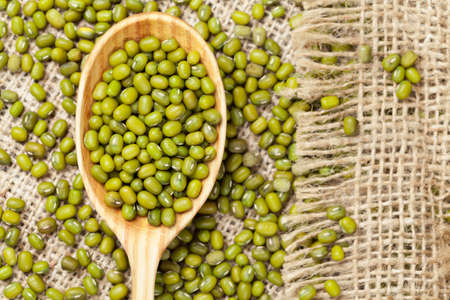 Heap of organic raw green mung bean lentils in wooden spoon on vintage textile backgroundの写真素材