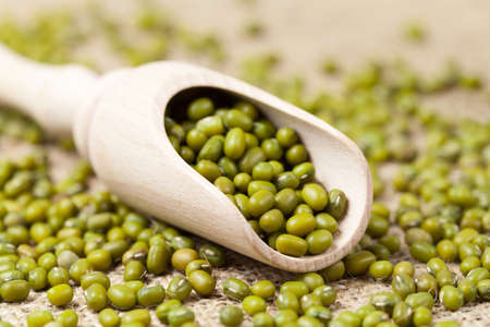 Heap of healthy uncooked organic mung beans vegetarian super foods in wooden spoon on vintage textile backgroundの写真素材