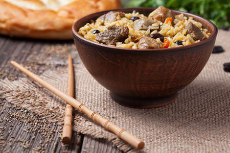 Traditional healthy asian national spicy rice food pilaf cooked with fried meat, onion, carrot and garlic. Served in rustic clay bowl on vintage wooden table backgroundの写真素材