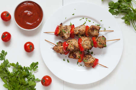 Grilled chiken kebab skewer barbecue meat with pepper and sauce on white dish.  Served on kitchen table background. Rustic style, natural light.の写真素材