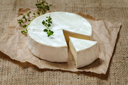 Camembert gourmet round cheese traditional French delicious dairy creamy meal  with thyme on rustic parchment and vintage sacking. Natural light, rustic style.の写真素材