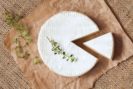 Sliced round camembert cheese traditional milk creamy dairy product with thyme on vintage parchment. Rustic style and natural light. Top view. Rustic sacking textile background.の写真素材