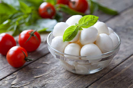 Traditional italian mozzarella cheese in glass bowl with basil and tomatoes caprese on rustic wooden background. Rustic style and natural light.の写真素材