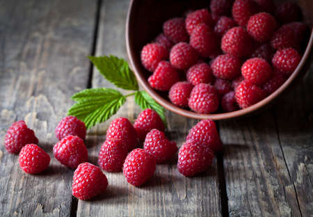 Fresh organic healthy raspberry with mint leaves in clay dish on vintage wooden table background....