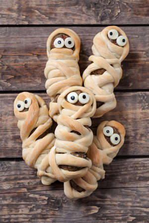 Scary halloween mummy sausages wrapped in dough with funny eyes for celebration party decoration. Vintage wooden background. Rustic style.の写真素材