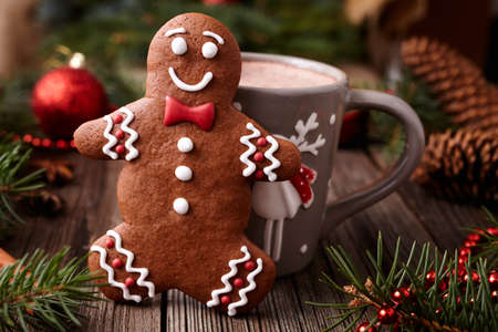 Cup of hot chocolate or cocoa beverage with cinnamon and gingerbread man cookie in new year tree decorations frame on vintage wooden table background. Homemade traditional celebration dessert recipeの写真素材