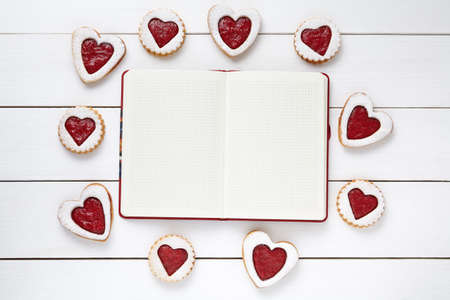 Empty notebook frame for design text and heart shaped cookies on white wooden background. Valentines day food concept of romantic love. Top view, flat lay.の写真素材