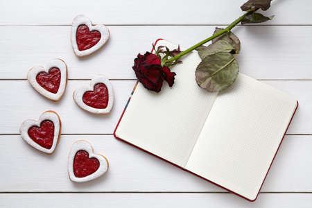 Heart shaped cookies with empty notebook frame and red rose gift composition for Valentines Day. Valentines day food concept of romantic love. Top view, flat lay.の写真素材