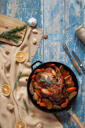 Barbecued whole chicken with crispy brown skin stuffed with vegetables and spices in black cast iron skillet on vintage wooden table background. Top view, rustic style.の写真素材