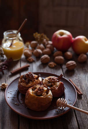 Baked stuffed apples with nuts and raisins in clay dish on vintage wooden table background. Healthy diet snack.の写真素材