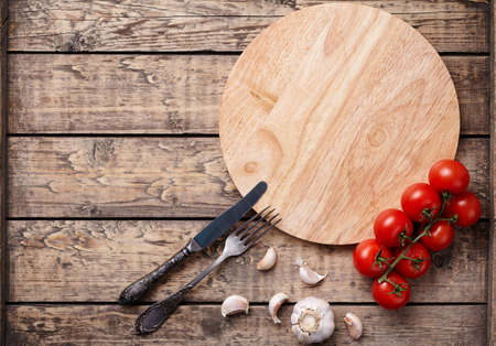 Pizza cutting board template with empty space for design text. Round wooden plate with tomatoes on vintage wooden background. Top view rustic style.の写真素材