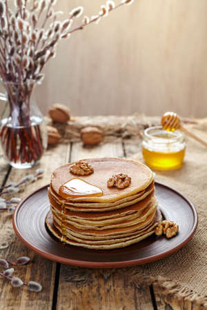 Stack of pancakes with flowing honey and nuts on vintage wooden table background. Traditional American dessert. Rustic style.の写真素材