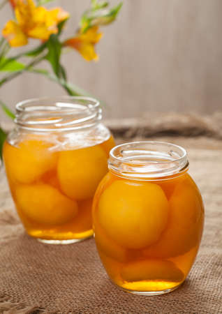 Canned natural peaches in glass jars with compote on vintage cloth backgroundの写真素材