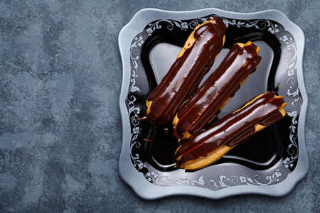 Eclairs with chocolate and whipped cream on black dish background. Traditional French dessert. Empty...