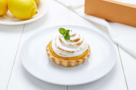 Lemon tart with whipped cream and mint sweet dessert on white plate