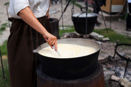 Woman prepare cornmeal, maize or quinoa porridge in cast iron cauldron or dutch oven. Lifestyle street foodの写真素材