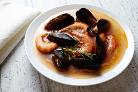 Fish seafood soup bouillabaisse. Mussels, shrimp, lobster in tomato sauce. The traditional dish of Marseilles. White wooden background.の写真素材