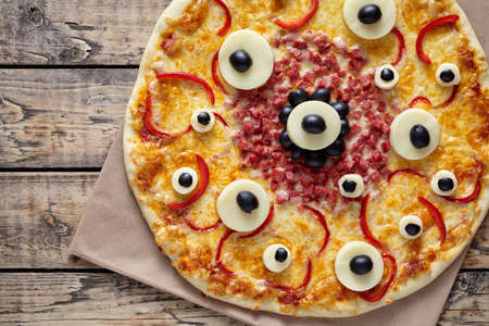 Halloween scary food monster pizza with eyes on vintage wooden table background. Traditional homemade celebration party decorationの写真素材