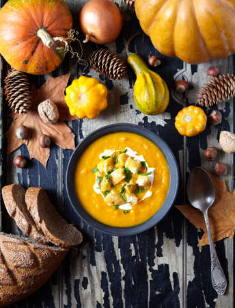 Pumpkin and carrot soup with cream, croutons on creative old dark wooden background. For Thanksgiving, halloween. Copy space. Top view. Composition of autumn vegetables.の写真素材