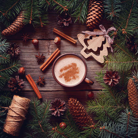 The warm winter drink. Cocoa or cappuccino in the winter festive vintage rustic decorations with Christmas tree and pine cones. Top view. Square format.の写真素材