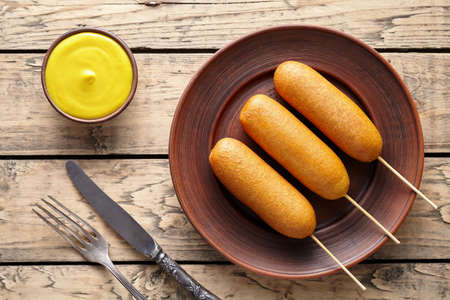 Corn dog traditional American street junk food deep fried hotdog meat sausage snack treat coated in a thick layer of cornmeal batter on stick unhealthy eating on rustic wooden background table.の写真素材