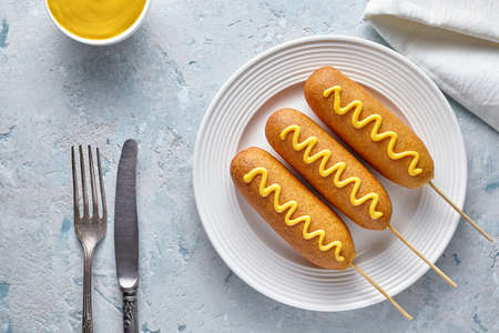 Corn dog traditional American corndog street junk food deep fried hotdog meat sausage with mustard on top snack treat coated in a layer of cornmeal batter on stick unhealthy eating on rustic table.の写真素材