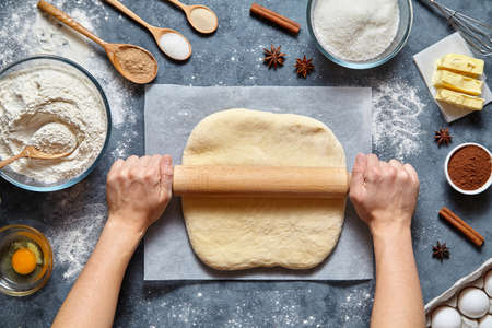 Dough bread, pizza or pie recipe homemade preparation. Female chef cook hands rolling dough with pin. Food ingridients flat lay on kitchen table. Working with pastry or bakery cooking. Top viewの写真素材