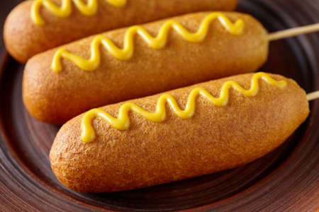 Corn dog street junk food deep fried hotdog meat sausage with mustard snack treat coated in a thick...