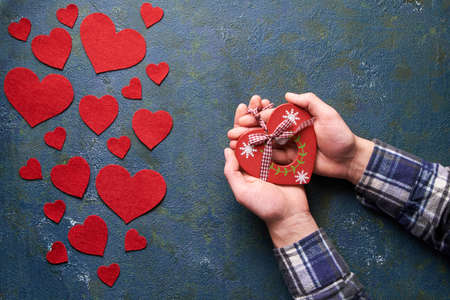 Man hands holding Valentine wooden heart toy. Concrete background with hearts and gifts on...