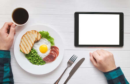 Healthy morning breakfast online shopping concept with tablet blank pure white screen for text or picture design. Mans hands with eggs, peas, bread and juice meal. Modern people lifestyle flat layの写真素材