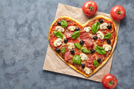 Heart shaped pizza love concept Valentines Day flat lay romantic dinner Italian food. Olives, prosciutto, champignons, tomatoes and mozzarella meal on blue table background.の写真素材
