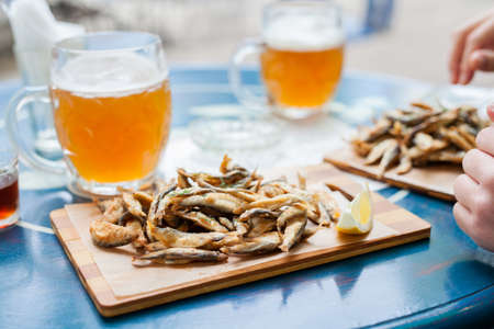 Fried small fish anchovy on board and beer on a blue table in the bar with a nautical theme. Spending fun time with great food.の写真素材