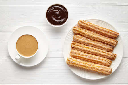 Churros traditional homemade Spain street fast food baked sweet dough snack with chocolate and coffee, white plate, white table background. Flat lay top viewの写真素材