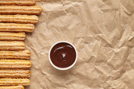 Churros traditional Spain breakfast or lunch street fast food baked sweet snack dessert with chocolate dipping on rustic decorative parchment paper background. Flat lay top viewの写真素材