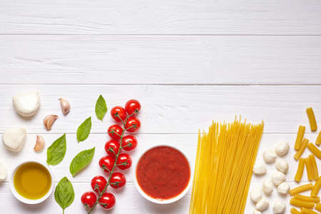 Traditional Italian food preparation background with empty copy design space on white wooden texture kitchen table. Basil, olive oil, tomato sauce, rolling pin, tomatoes. Flat lay, top view.