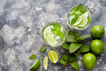 Mojito traditional cuban highball cocktail alcohol drink, top view copy space, summer tropical vacation beverage with rum, peppermint mint, lime juice, soda water, sugar and ice on concrete backgroundの写真素材