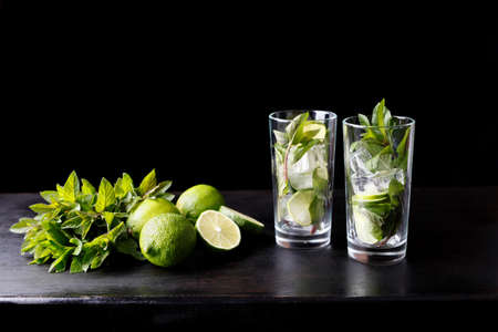 Mojito traditional refreshing cocktail alcohol drink in glass bar preparation with lime, mint leaves, sugar, and rum. Dark black background with copy space for textの写真素材
