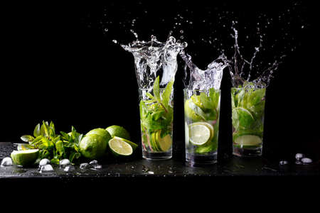 Mojito summer beach refreshing tropical cocktail splash in glass highball alcohol drink with soda water, lime juice, mint leaves, sugar, ice and rum. Dark black background with copy space textの写真素材