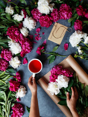 Florist at work. A woman in the process of making a summer bouquet of peonies, holds in her hand a cup of tea karkade. Tools and accessories florists need for making up a bouquet.の写真素材