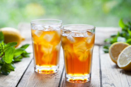 Ice tea summer refreshing cocktail drink on wooden table with a view to the terrace and trees. Close up summer antioxidant beverage. A frozen glass. Cold longdrink or lemonadeの写真素材