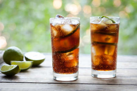 Cuba Libre refreshing summer cocktail with a cola, ice, lime and rum on wooden table with a view to...