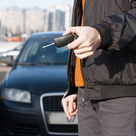 Male holding car keys with car on background