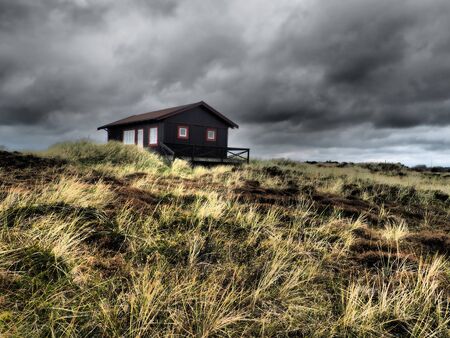 Traditional wooden hut in the middle of a meadow in northern Europe moments before a storm beginsのeditorial素材